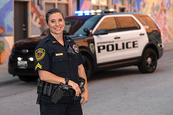 female police officer posed in front of police vehicle with lights on