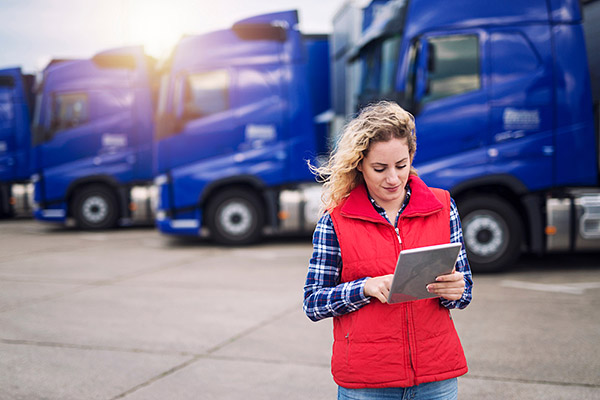 lady looking down at tablet while standing in front of several semi trucks