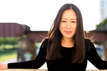 Korean American lady faces camera with arms stretched out on fence