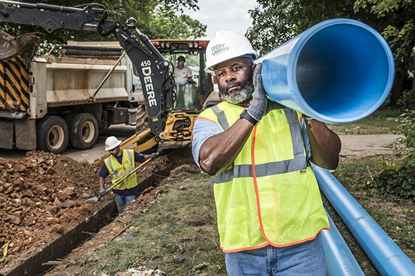 utility worker carrying a large blue pipe on his shoulder