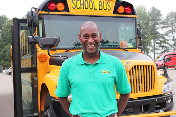 smiling male driver standing in front of a yellow school bus